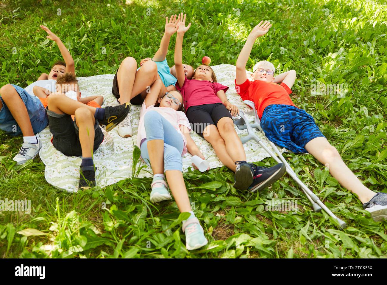 Männliche und weibliche Freunde liegen auf einer Decke mit erhobener Hand im Park Stockfoto