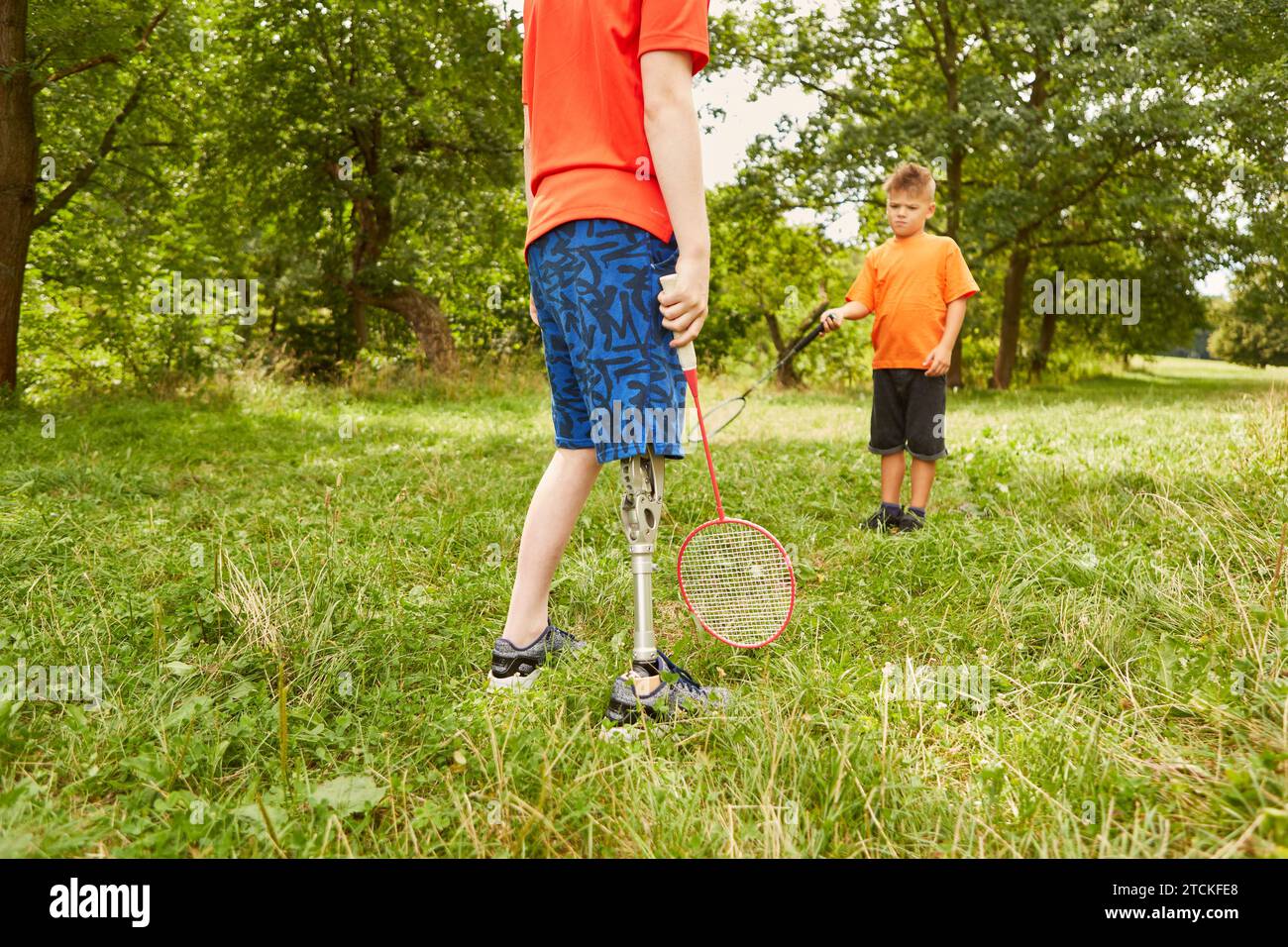 Behinderter Junge, der Badminton mit einem männlichen Freund spielt, während er im Park steht Stockfoto