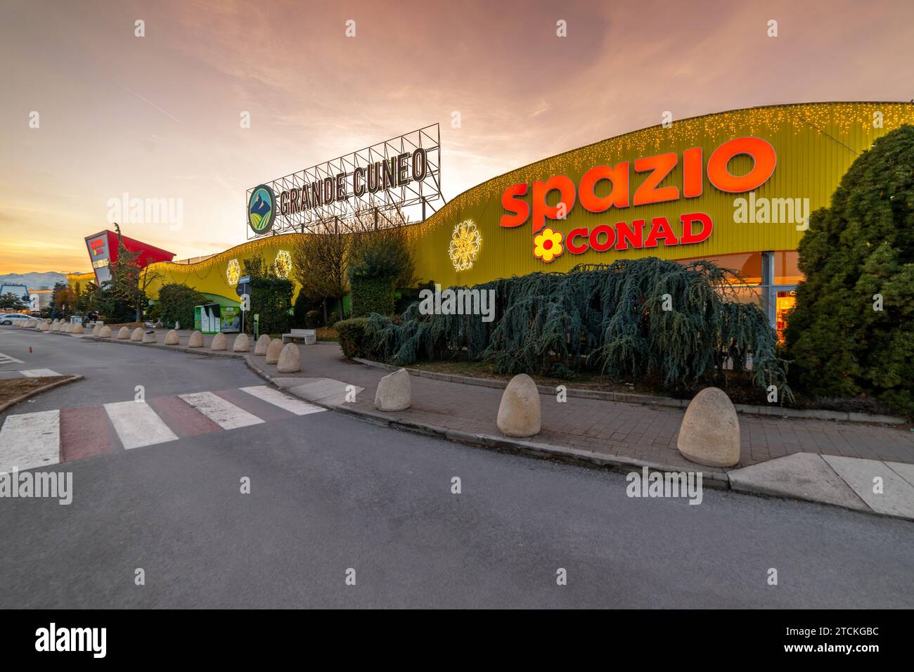 Cuneo, Italien - 12. Dezember 2023: Außenfassade des Einkaufszentrums Grande Cuneo mit Spazio Conad Hypermarktschild und dekorativen Weihnachtslichtern mit Sonne Stockfoto