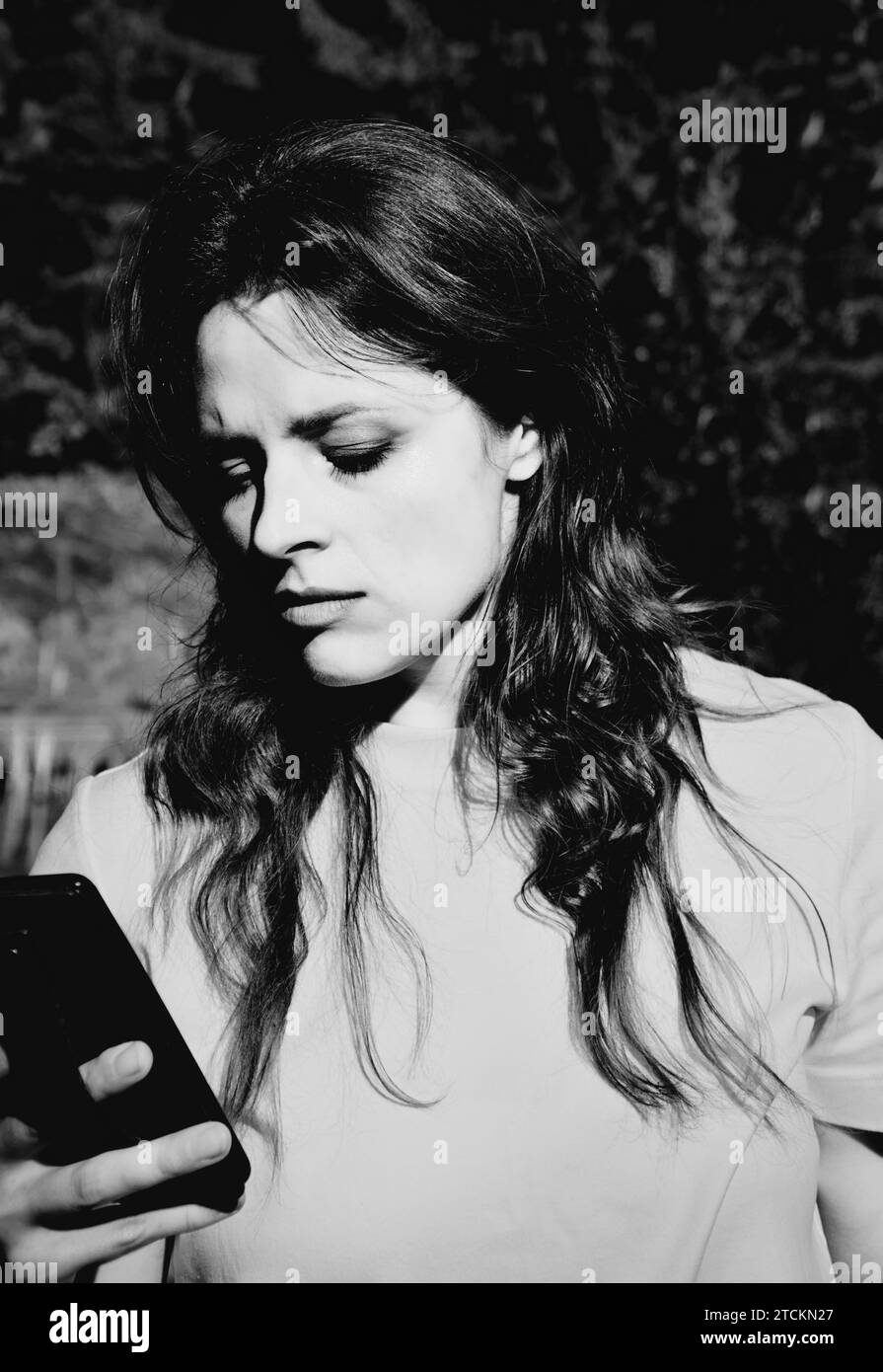 Schwarz-weiß-Bild einer Frau, die die Stirn runzelt und auf ihren Smartphone-Bildschirm blickt Stockfoto