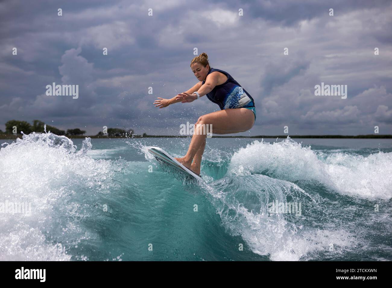 Eine Frau, die aggressiv auf einem Surfbrett auf einer Bootswache reitet. Stockfoto
