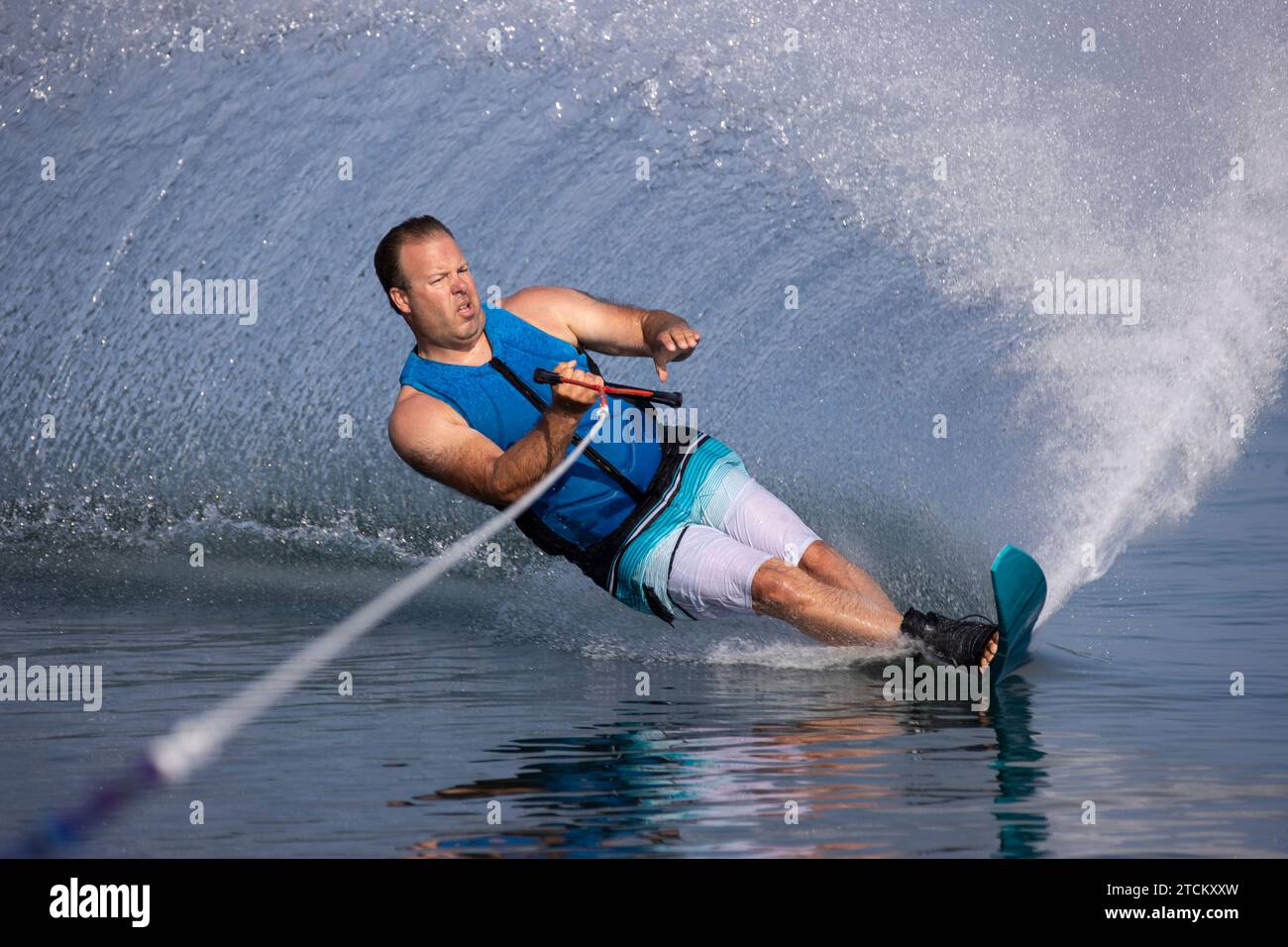 Ein Mann, der eine enge Kurve auf einem Slalom-Wasserski macht und großen Sprühnebel wirft. Stockfoto