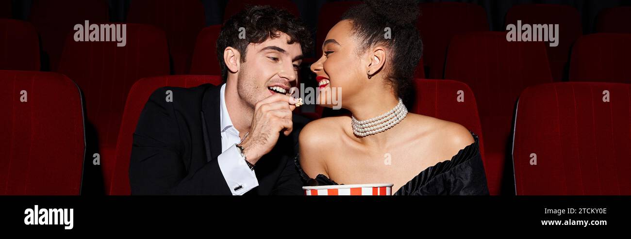 Hübscher Mann, der Popcorn mit seiner hübschen afroamerikanischen Freundin teilt, bei einem Date im Kino, Banner Stockfoto