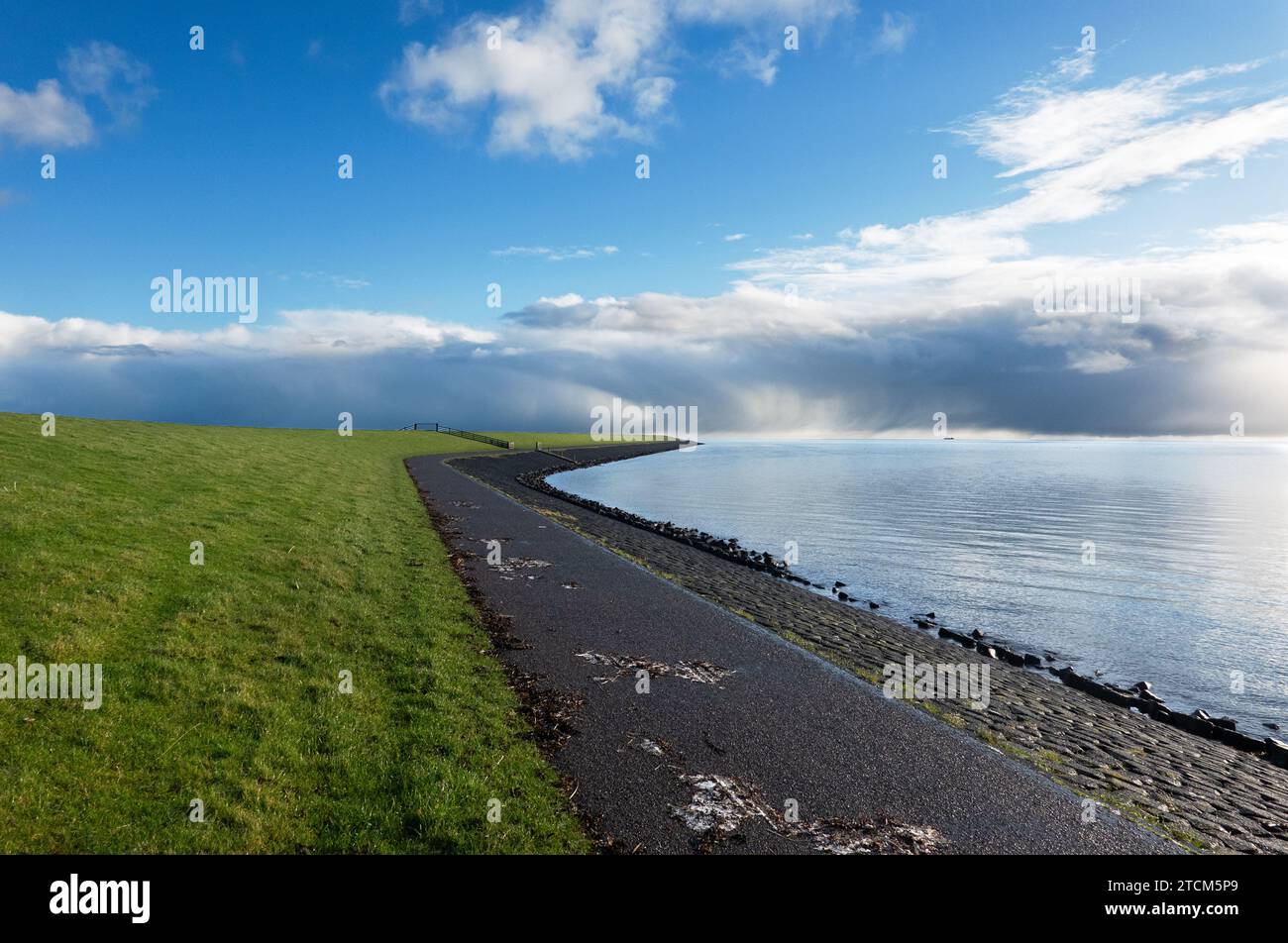 Langer, gerader Deich, Gras, Basaltblöcke und ein Radweg Stockfoto