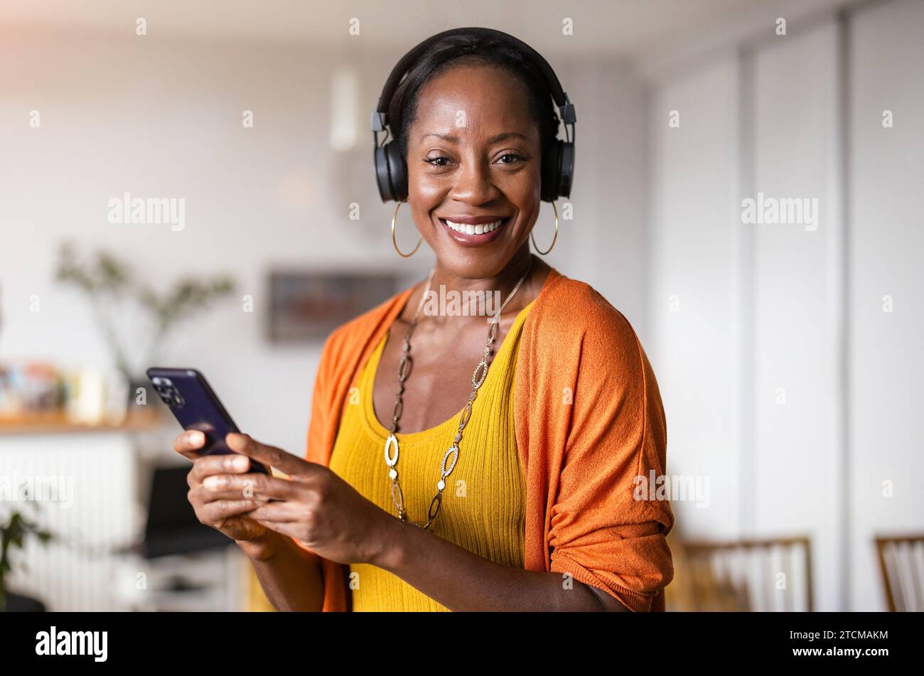 Frau hört Musik mit Kopfhörern, die mit ihrem Smartphone verbunden sind, im Wohnzimmer zu Hause Stockfoto