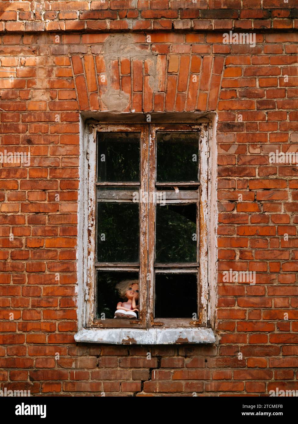 Die alte Puppe schaut aus dem Fenster des alten Ziegelhauses. Stockfoto