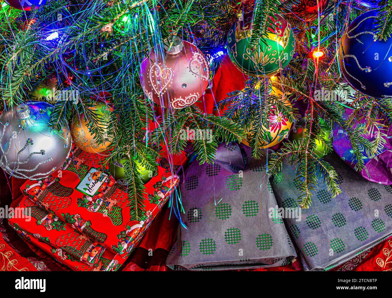 Geschenke unter dem Weihnachtsbaum. Zweige mit Dekoration und Weihnachtskugeln. Weihnachtsbaumbeleuchtung. Stockfoto