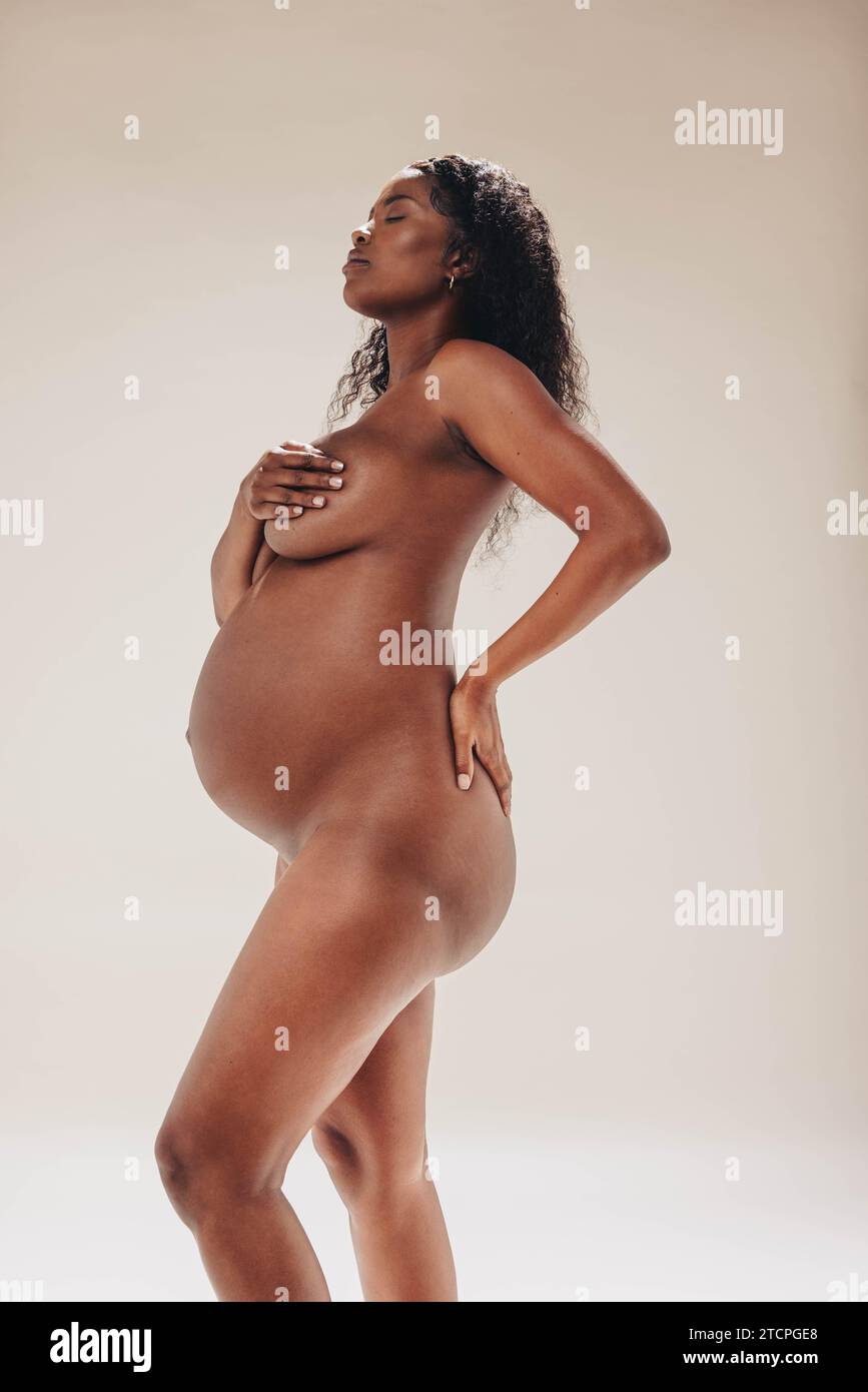 Eine selbstbewusste schwarze Frau zeigt stolz ihre Baby-Beule während des dritten Trimenons ihrer Schwangerschaft. Sie feiert Körperpositivität und Mutterschaft, sie stan Stockfoto