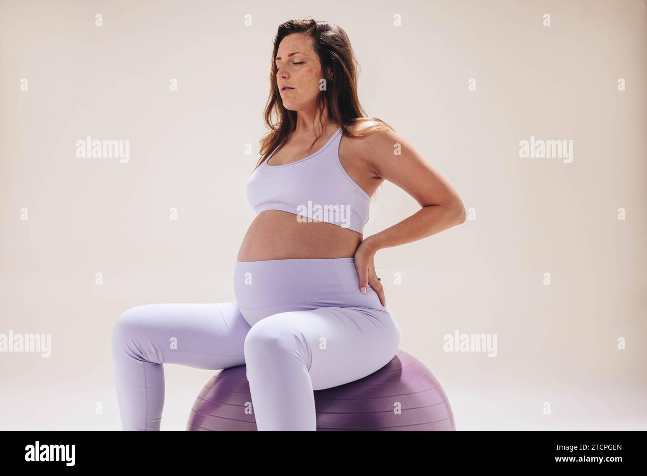 Eine schwangere Frau im dritten Trimenon übt pränatalen Yoga in einem Studio und benutzt einen Trainingsball für Stabilität. Teilnahme an Atemübungen und en Stockfoto