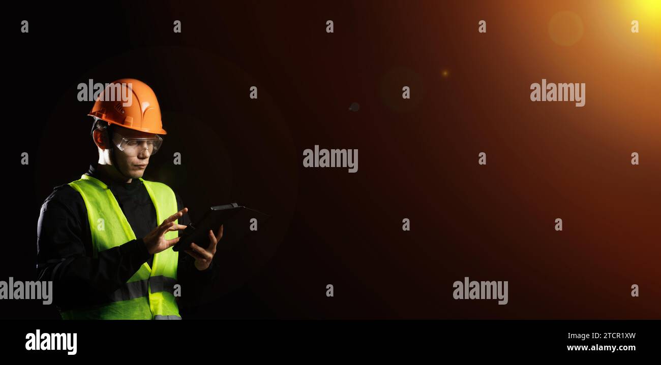 Engineering Consulting, ein männlicher Bauarbeiter in einem Schutzhelm auf dunklem Hintergrund benutzt ein Tablet. Geschäftsprozessmanagement und Bauinspektor mit Stockfoto