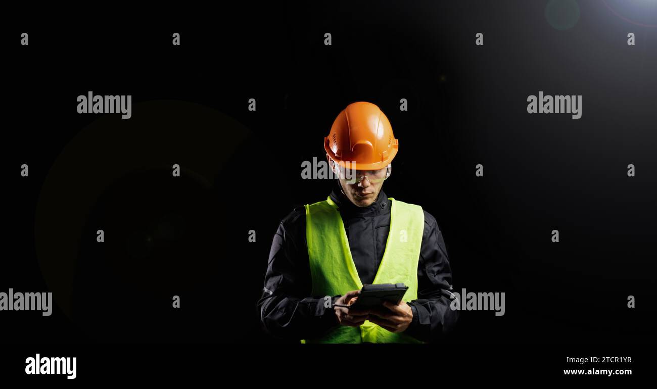 Engineering Consulting, ein männlicher Bauarbeiter in einem Schutzhelm auf dunklem Hintergrund benutzt ein Tablet. Geschäftsprozessmanagement und Bauinspektor mit Stockfoto