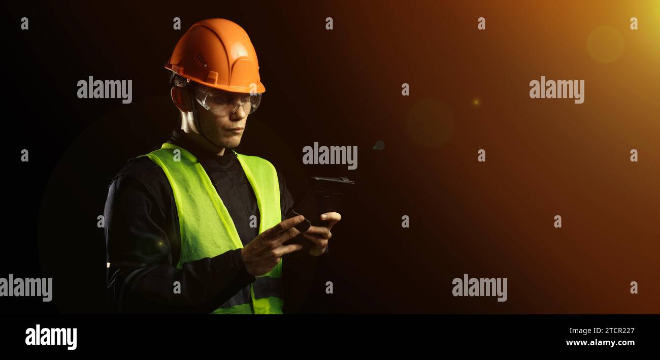 Engineering Consulting, ein männlicher Bauarbeiter in einem Schutzhelm auf dunklem Hintergrund benutzt ein Tablet. Geschäftsprozessmanagement und Bauinspektor mit Stockfoto
