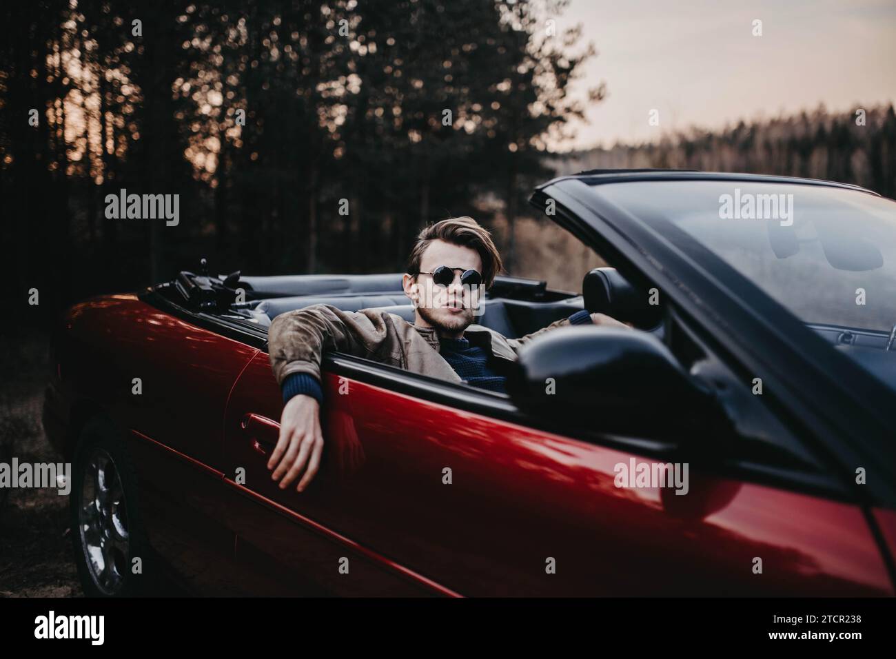 Cooler Mann in Sonnenbrille in einem roten Cabrio in der Natur, ein reicher arroganter Mann Stockfoto