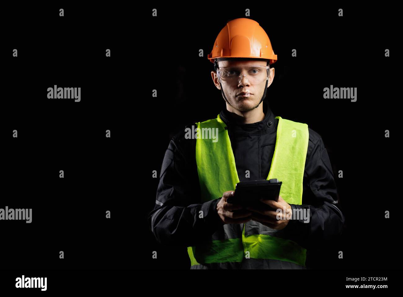 Engineering Consulting, ein männlicher Bauarbeiter in einem Schutzhelm auf dunklem Hintergrund benutzt ein Tablet. Geschäftsprozessmanagement und Bauinspektor mit Stockfoto