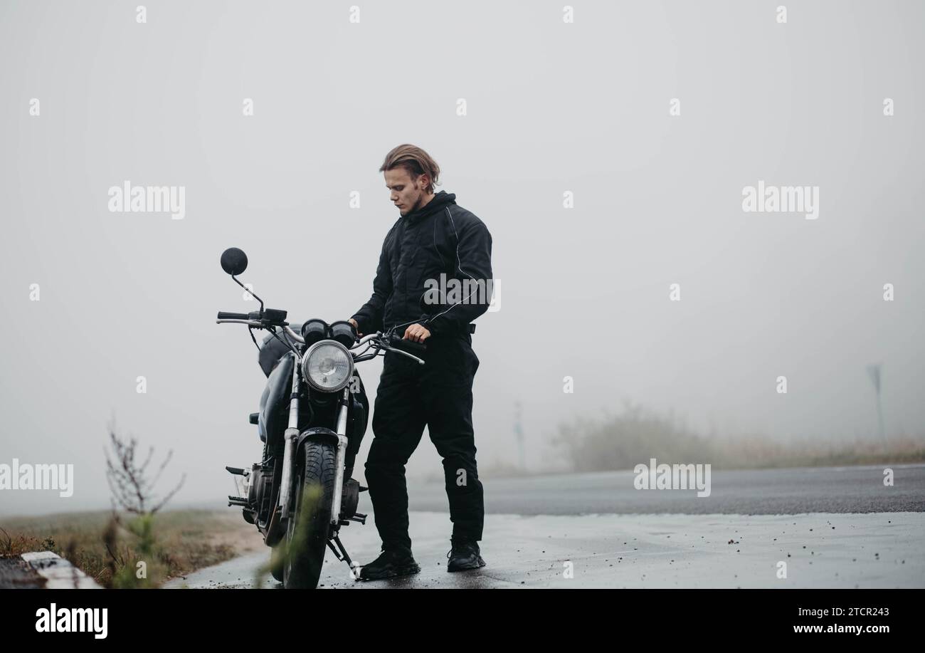 Motorradfahrer männlicher Biker auf einer nebeligen Straße mit einem Motorrad im Herbst bei regnerischem Wetter, das Konzept der Ausrüstung für einen Motorradfahrer Stockfoto