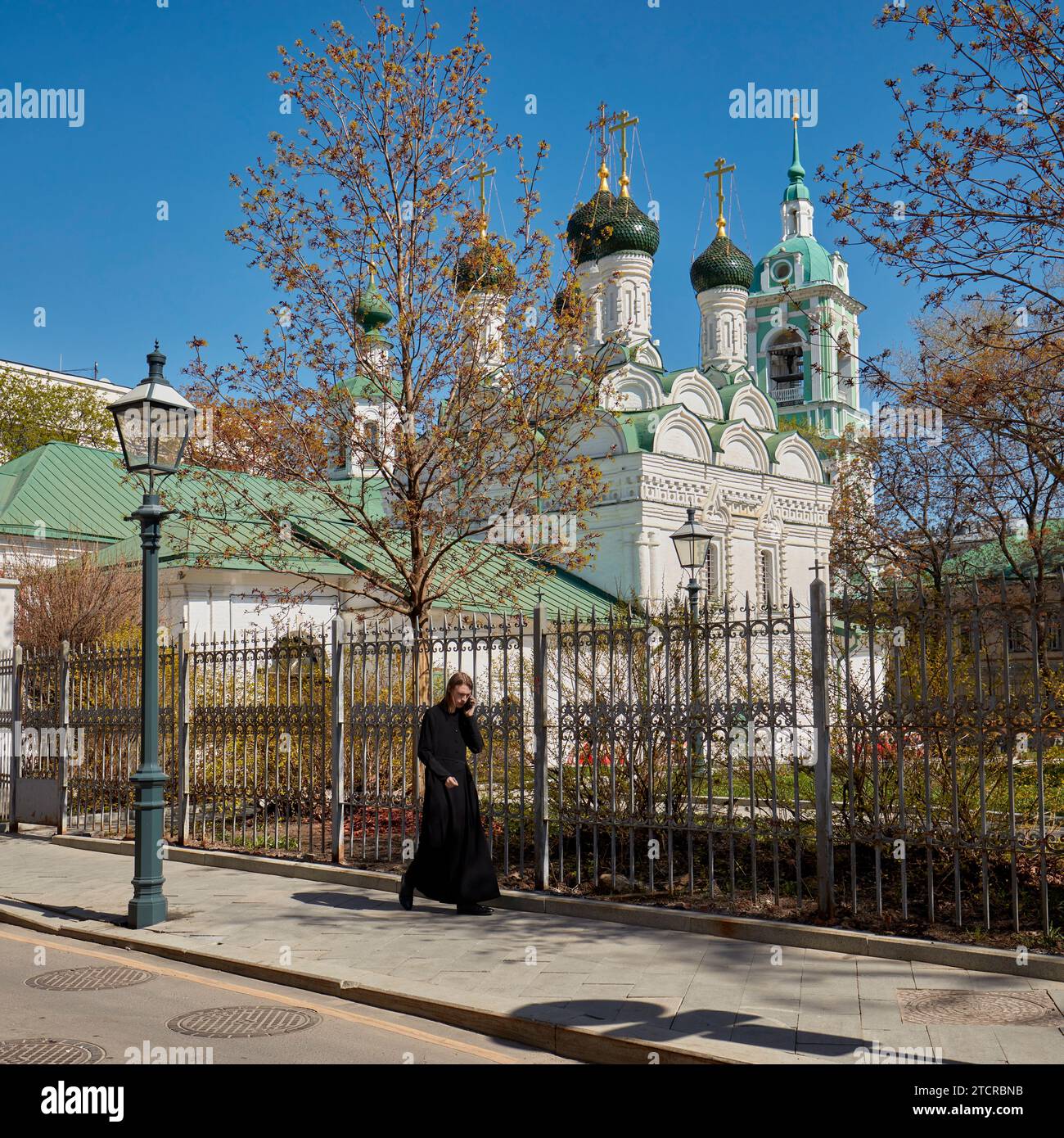 Junger Mann in schwarzem Gewand, der an der Kirche der Enthauptung Johannes des Täufers von Bohr vorbeigeht, während er über sein Handy redet. Moskau, Russland. Stockfoto