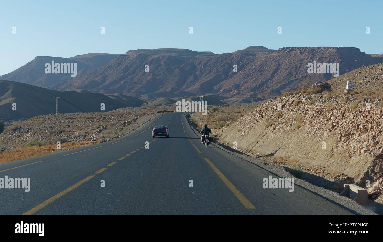 Auto und Motorrad auf einer Straße mit gelben Linien im Atlasgebirge östlich von Marrakesch, Marokko, 13. Dezember 2023 Stockfoto