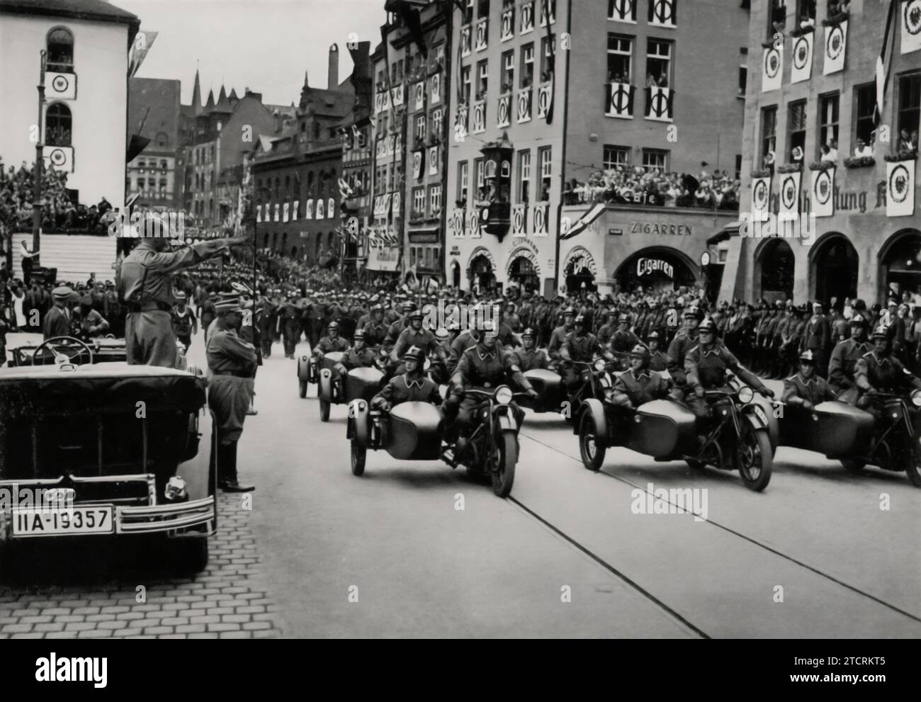 Beim Reichsparteitag 1935 sieht man Adolf Hitler in seinem offenen Auto stehen und die motorisierten SA-Sturmabteilung grüßen. Dieses Bild fängt einen Moment der Interaktion zwischen Hitler und der SA ein und betont die Rolle der Motorisierung im NS-Militärapparat. Hitlers Gruß aus dem Auto, ein Symbol für seine Führung und die Modernisierungsbemühungen des Regimes, unterstreicht die Bedeutung der SA für die Demonstration der Stärke und Einheit der Partei während dieser großen, stark choreografierten Ereignisse. Stockfoto