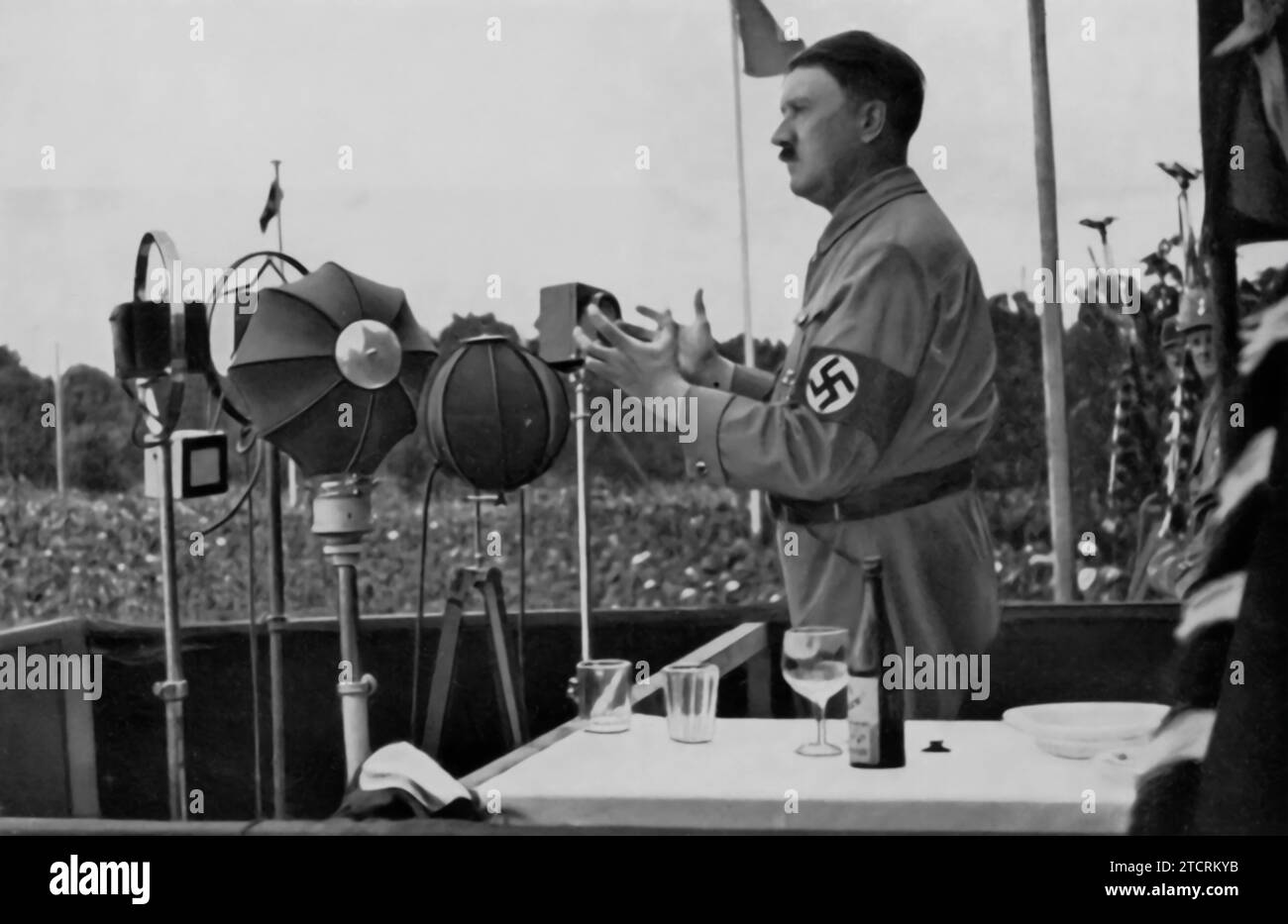 Adolf Hitler ist dargestellt, das sich an das deutsche Volk wendet, ein Bild, das seine häufigen öffentlichen Reden repräsentiert, die für die Öffentlichkeitsarbeit und Propaganda des NS-Regimes von zentraler Bedeutung waren. Diese Reden, die oft landesweit ausgestrahlt wurden, waren der Schlüssel zur direkten Vermittlung der NS-Politik und -Ideologie an die Bevölkerung. Hitlers Ansprachen sollten nationale Gefühle ansprechen, Unterstützung für die Ziele des Regimes sammeln und seine Position als vereinigender Führer Deutschlands stärken. Stockfoto