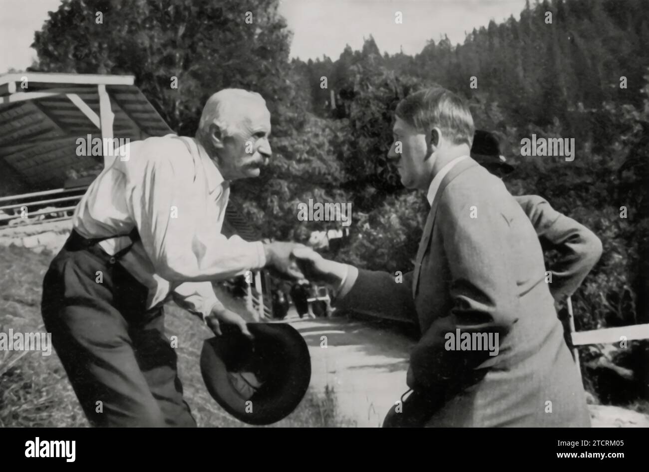 Adolf Hitler wird auf dem Obersalzberg dargestellt und schüttelt einem älteren Nachbarn die Hand. Dieses Bild soll Hitler in einem sympathischen und zugänglichen Licht darstellen und auf freundliche Weise mit den Anwohnern interagieren. Der Handschlag mit einem älteren Herrn in seiner Residenz unterstreicht die Verbindung zur Gemeinschaft, eine Szene, die geschaffen wurde, um einen fundierteren und nachvollziehbaren Aspekt seiner Führung der Öffentlichkeit zu präsentieren. Stockfoto