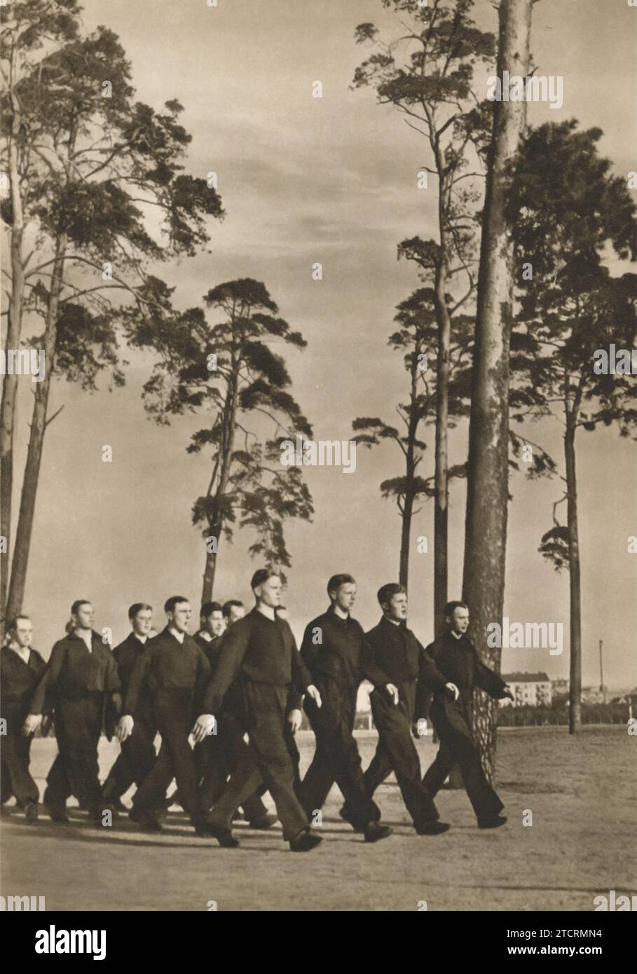 Deutsche Rekruten werden in einem lebendigen Moment gefangen gehalten, singen zusammen, während sie auf dem Weg zum morgendlichen Sporttraining marschieren. Diese Praxis des unisono-Gesangs fördert nicht nur die Moral, sondern stärkt auch das Gefühl der Einheit und Kameradschaft unter den Rekruten. Die Szene veranschaulicht einen wichtigen Aspekt der militärischen Kultur, in der körperliche Fitness mit Teambuilding-Aktivitäten verwoben ist und ein temperamentvoller Ton für das Training des nächsten Tages gesetzt wird. Stockfoto