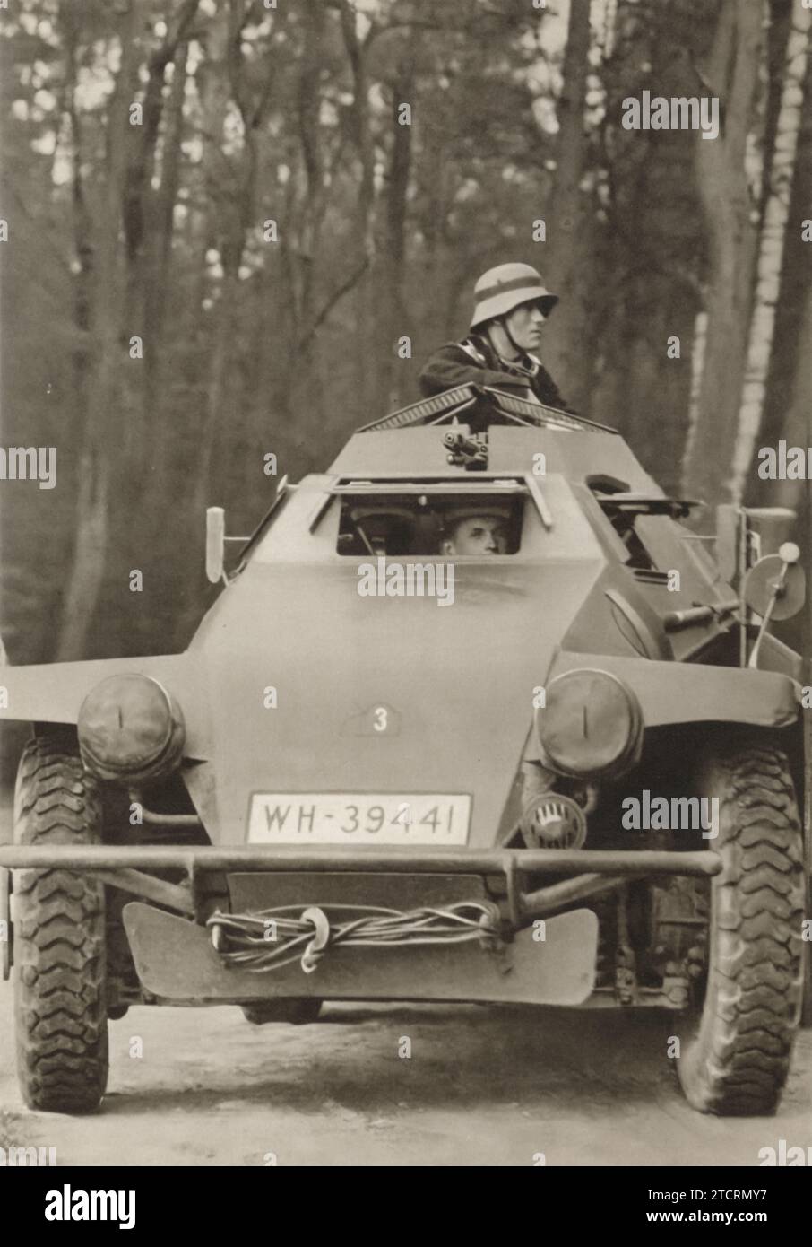 In einem kompakten gepanzerten Fahrzeug übernehmen deutsche Soldaten ihre Rollen: Eine als Fahrer, sichtbar durch die Frontluke, und eine andere als Hauptschützen, der eine leichte Maschinenpistole (LMG) von oben aus bedient. Diese effiziente Raumnutzung und Aufgabenverteilung war charakteristisch für die Panzerfahrzeugkonstruktion des deutschen Militärs in der Zeit um den Zweiten Weltkrieg Stockfoto