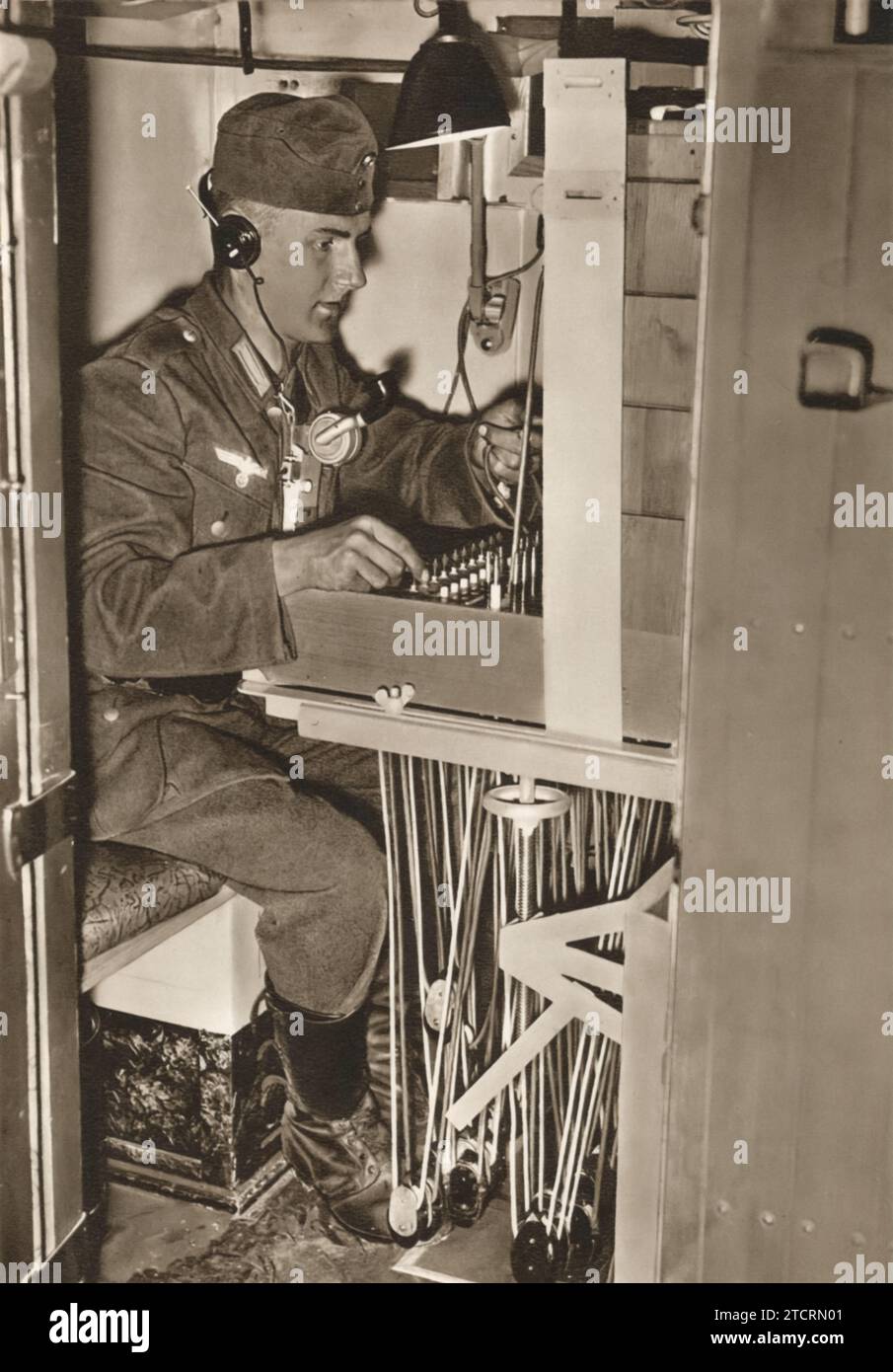 In diesem Bild ist ein deutscher Soldat dargestellt, der ein Kommunikationsgerät in einem speziell konstruierten Einsatzfahrzeug bedient. Seine Rolle ist die Übertragung von Telefonsignalen, eine entscheidende Funktion während des Zweiten Weltkriegs Die Fähigkeit, klare Mitteilungen zu senden und zu empfangen, war für die Koordinierung militärischer Maßnahmen und die Weiterleitung von Befehlen von entscheidender Bedeutung. Stockfoto