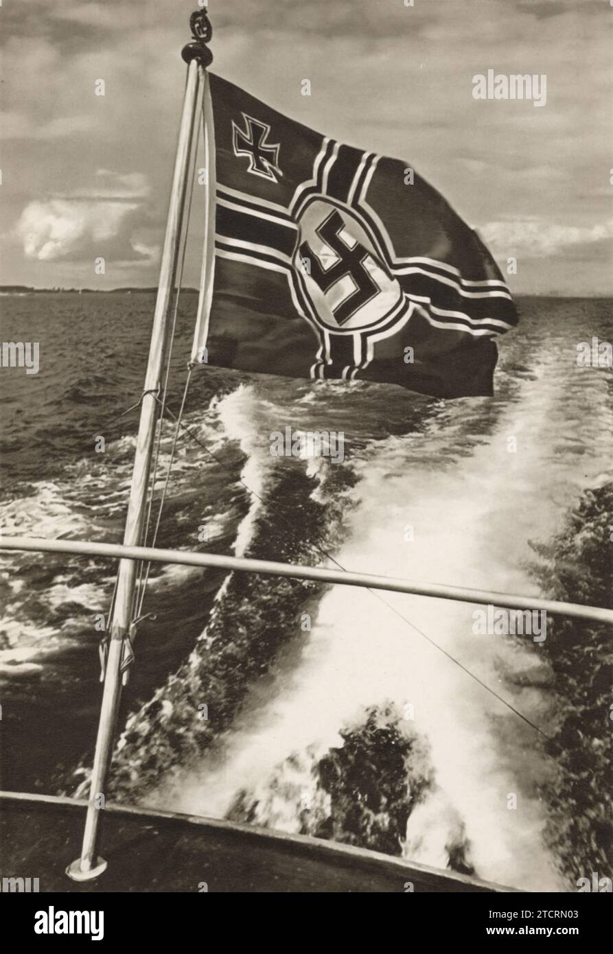 Das Bild zeigt eine deutsche Kriegsflagge, die auf der Rückseite eines Bootes in offenen Gewässern sichtbar ist. Das Vorhandensein der Flagge und das Design des Bootes deuten darauf hin, dass es Teil der deutschen Marine, der Kriegsmarine, ist, die während des Zweiten Weltkriegs aktiv war Die Kriegsmarine spielte eine wichtige Rolle in der deutschen Militärstrategie, da ihre Flotte in verschiedenen Marineschuhen operierte. Die Flagge, ein Symbol für die militärische Präsenz der Nation, wurde typischerweise auf solchen Schiffen geflogen, um ihre Loyalität und operative Identität zu signalisieren. Stockfoto