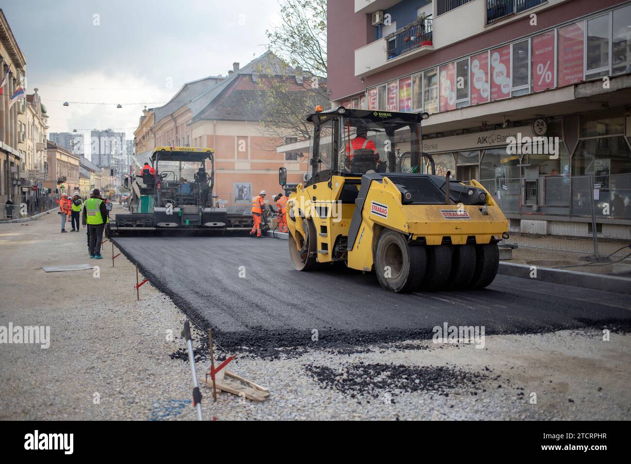 Belgrad, Serbien, 9. Dezember 2023: Asphaltpflastermaschine und pneumatische Walze legen neuen Asphalt entlang der Straße, die gerade rekonstruiert wird Stockfoto