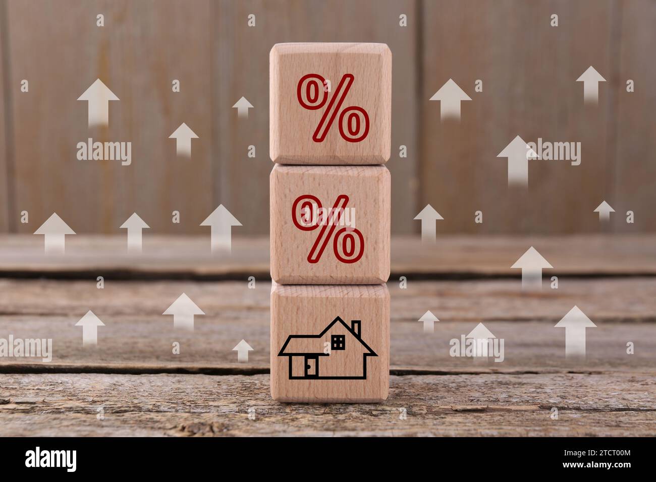 Steigende Hypothekenzinsen, dargestellt durch Aufwärtspfeile und Prozentzeichen. Würfel mit Haussymbol auf Holztisch Stockfoto