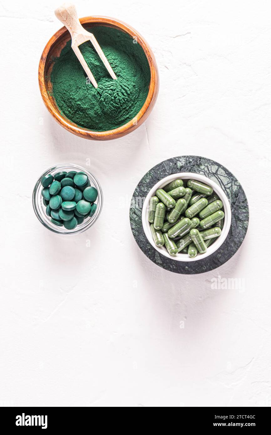 Grüne Spirulina-Algenpulver, Kapseln und Tabletten in Gläsern auf weißem geprägtem Hintergrund. Vertikale Ansicht. Eine Kopie des Bereichs. Entgiftung Stockfoto