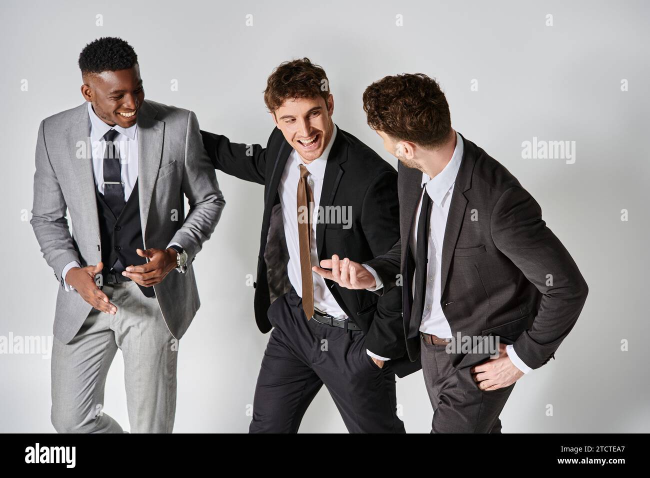 Junge glückliche multikulturelle Freunde in eleganten Geschäftskleidung, die fröhlich auf grauem Hintergrund lächeln Stockfoto