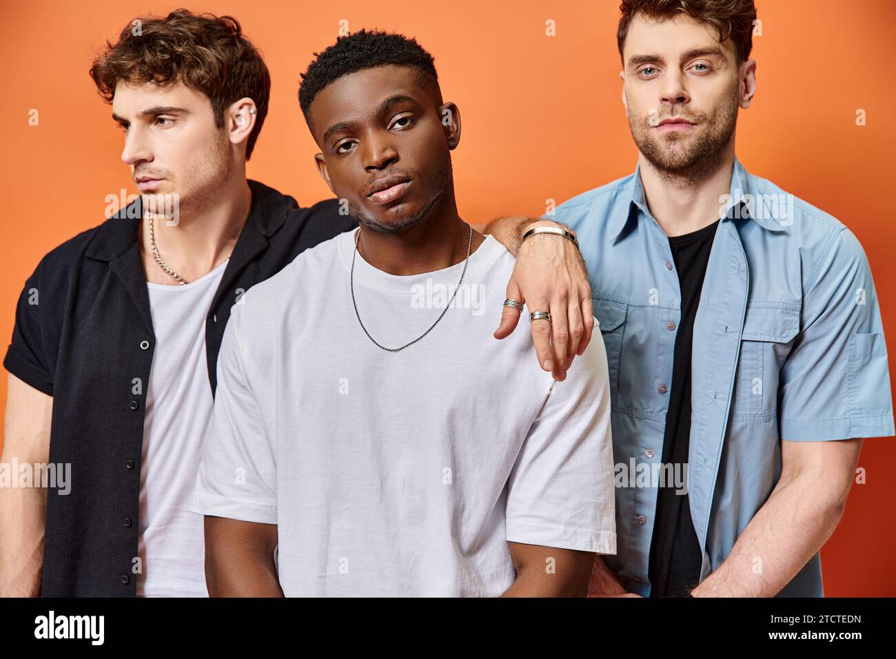 Gut aussehende, multirassische männliche Models in Straßenbekleidung, mit Blick auf die Kamera vor orangefarbenem Hintergrund, Mode Stockfoto