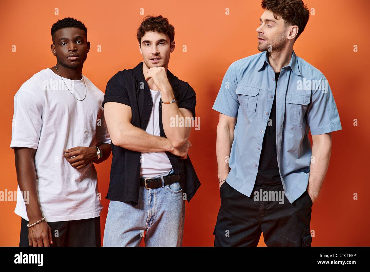 Gut aussehende, multirassische männliche Models in stilvoller Stadtkleidung, die vor orangefarbenem Hintergrund posieren Stockfoto