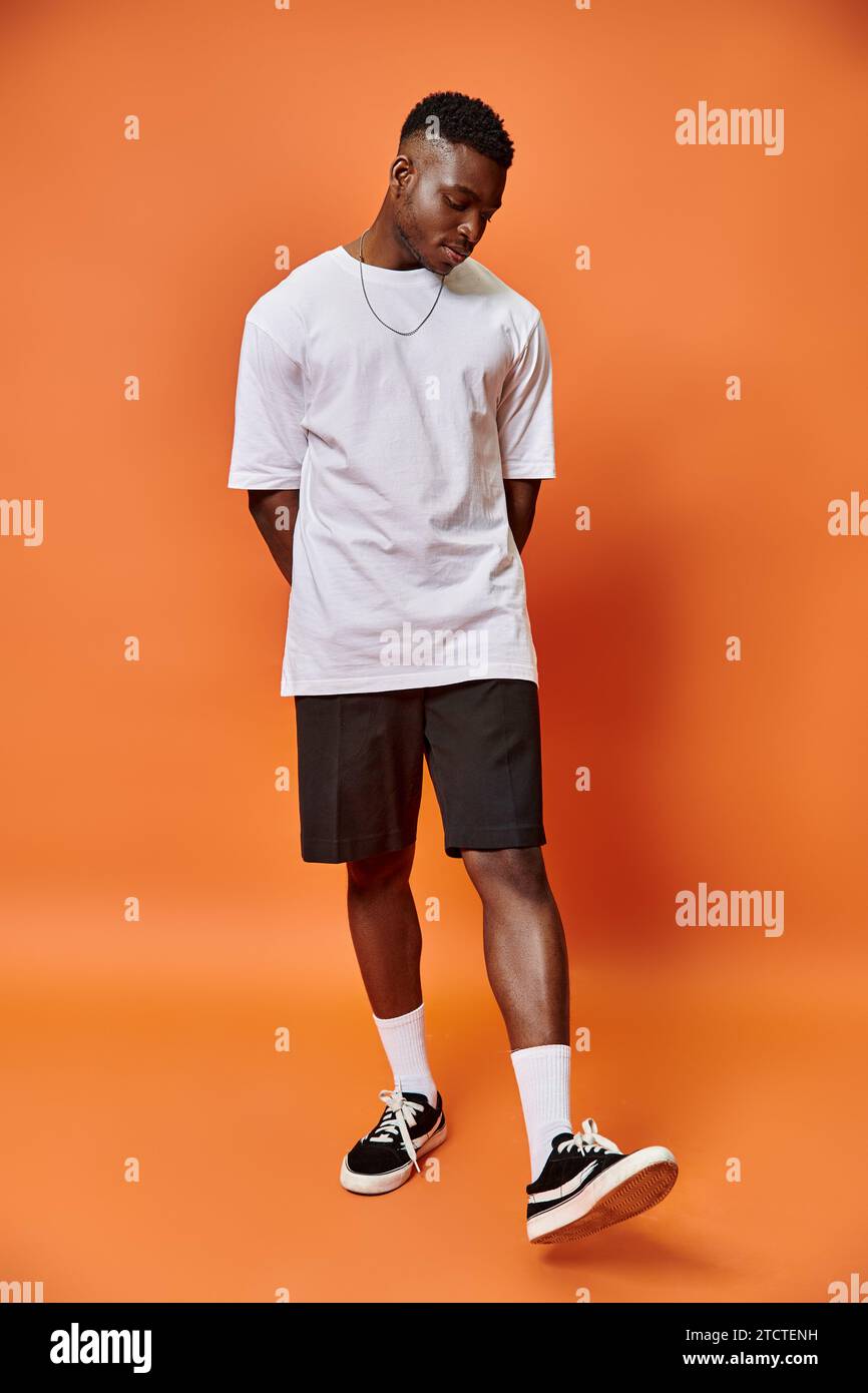 Attraktiver junger afroamerikanischer Mann im lässigen Outfit auf der Straße vor orangefarbenem Hintergrund, Modekonzept Stockfoto