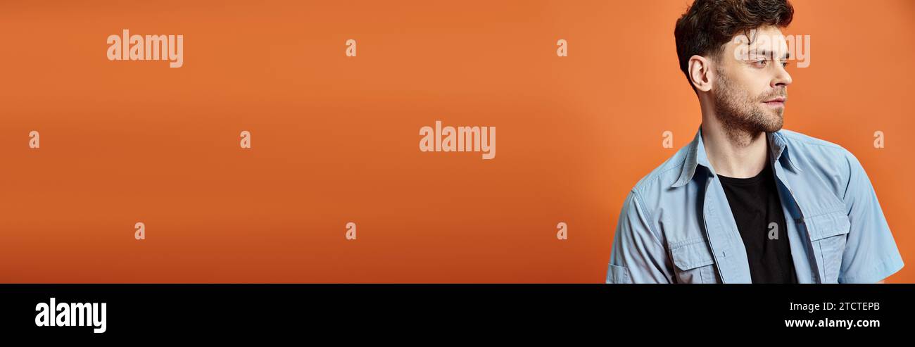 Ansprechender Mann in lässigem, trendigem Outfit vor orangefarbenem Hintergrund mit Blick auf die Kamera, Modekonzept Stockfoto