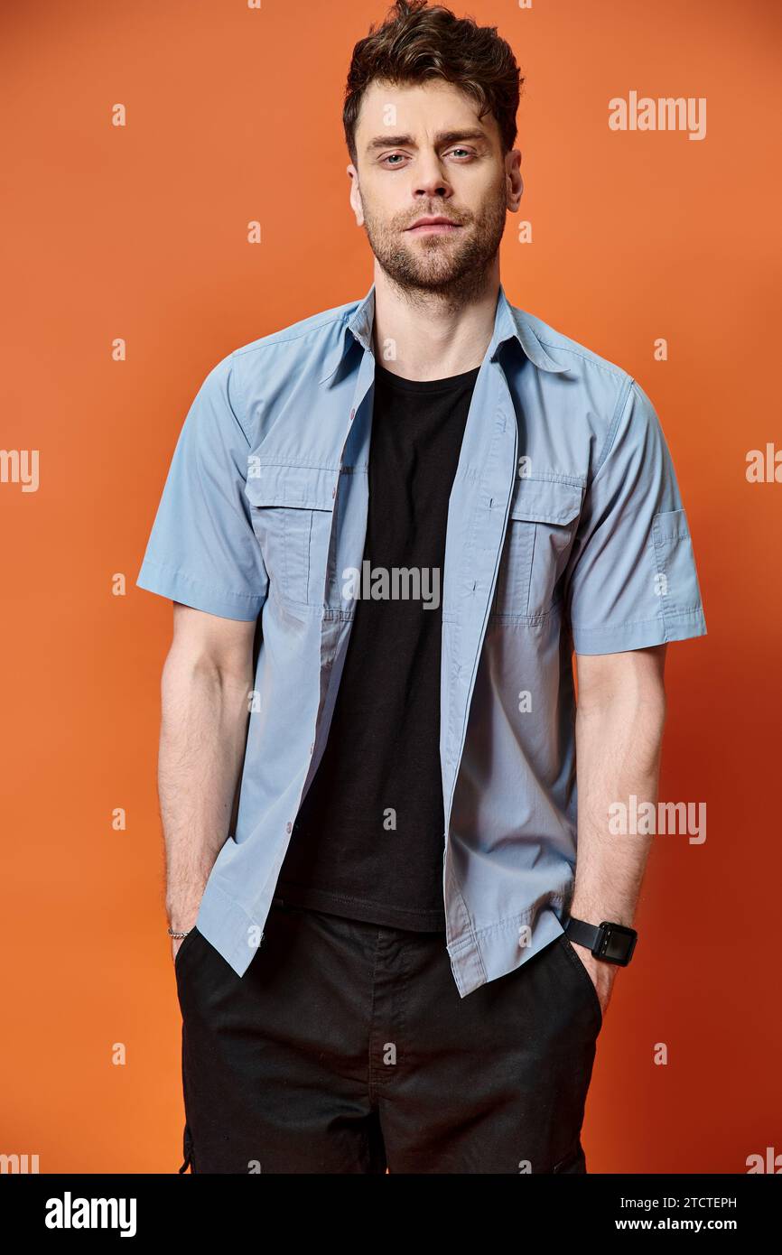 Hübscher Mann in lässigem, trendigem Outfit vor orangefarbenem Hintergrund mit Blick auf die Kamera, Modekonzept Stockfoto