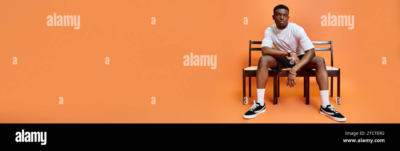 Hübscher junger afroamerikaner in urbanem Outfit, der auf der Bank sitzt, Modekonzept, Banner Stockfoto