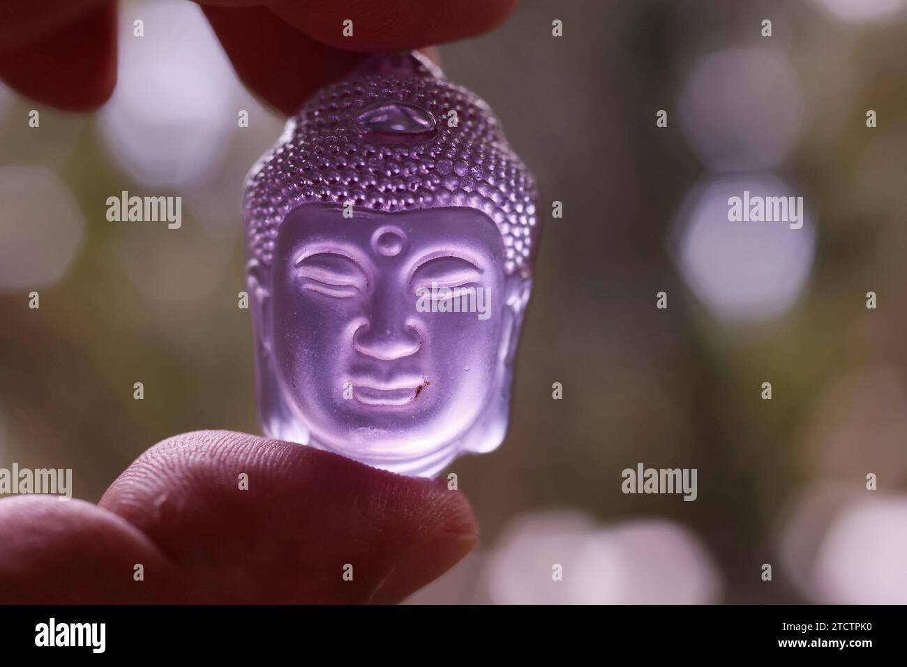 Violetter Buddha-Kopf-Anhänger in der Hand. Buddhistisches Symbol. Stockfoto