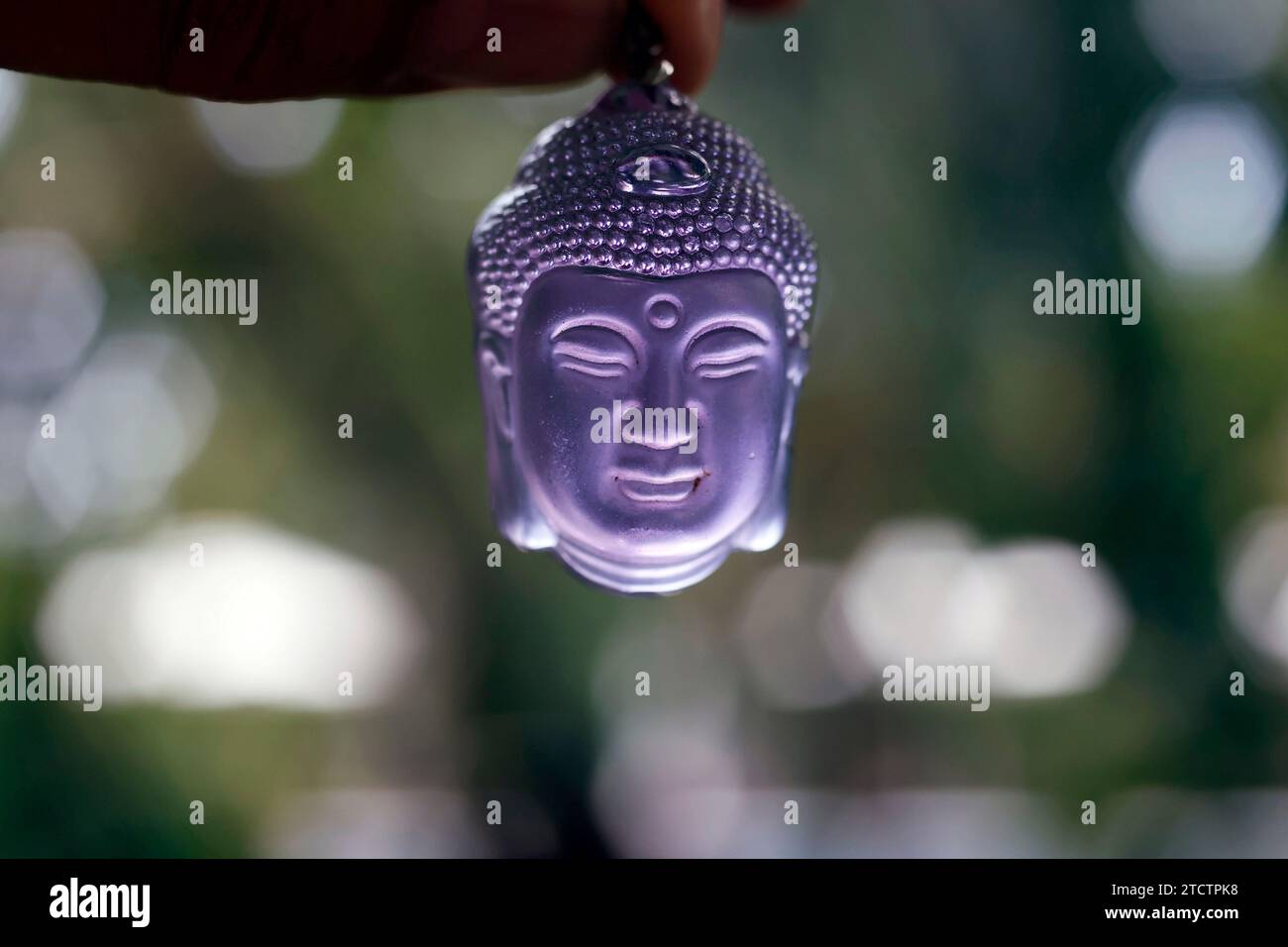 Violetter Buddha-Kopf-Anhänger in der Hand. Buddhistisches Symbol. Stockfoto