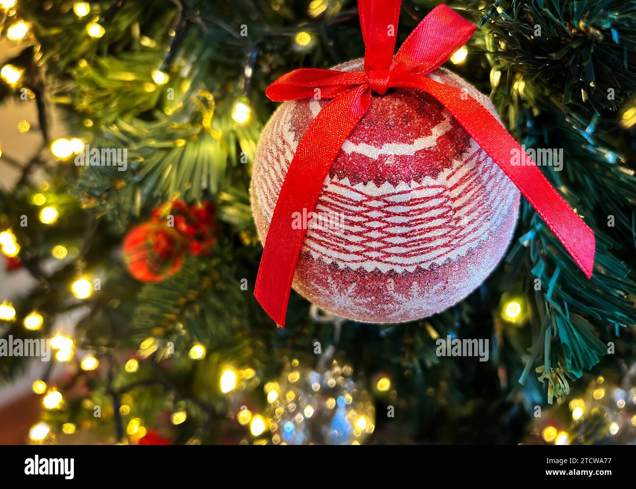 Nahaufnahme einer roten Kugel auf einem Weihnachtsbaum mit unscharfen Lichtern im Hintergrund, geringe Schärfentiefe. Weihnachts- und Neujahrskonzept. Stockfoto