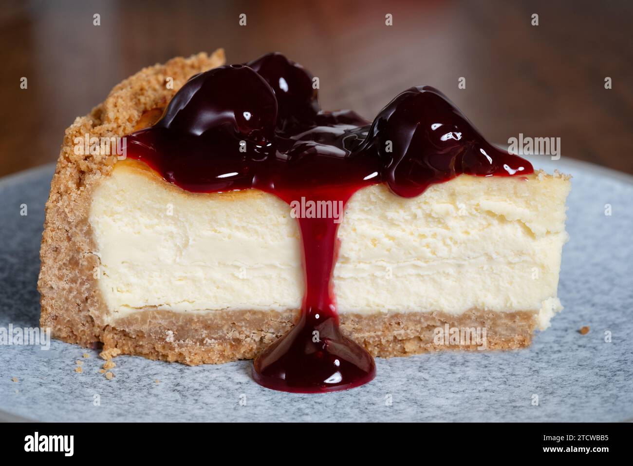 Eine in Scheiben geschnittene Portion eines tiefgefüllten New Yorker Käsekuchens mit schwarzen Kirschen. Der Kuchen wird auf Teller serviert. Stockfoto