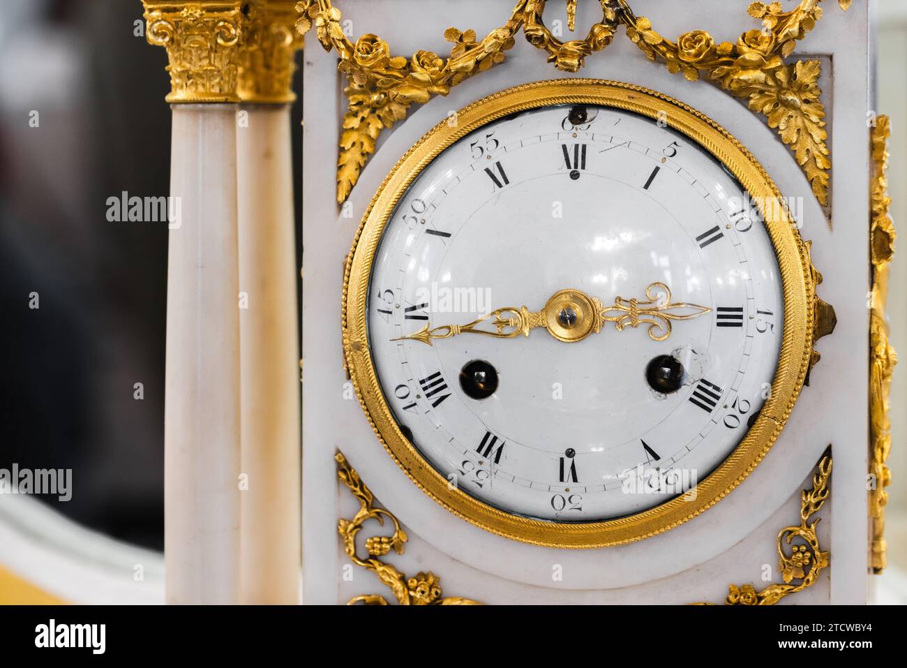 Vintage-Kaminuhr, Nahaufnahme, Vorderansicht. Uhr aus weißem Emaille mit römischen Ziffern und goldenen Zeigern, Zeitmesser im Barockstil Stockfoto