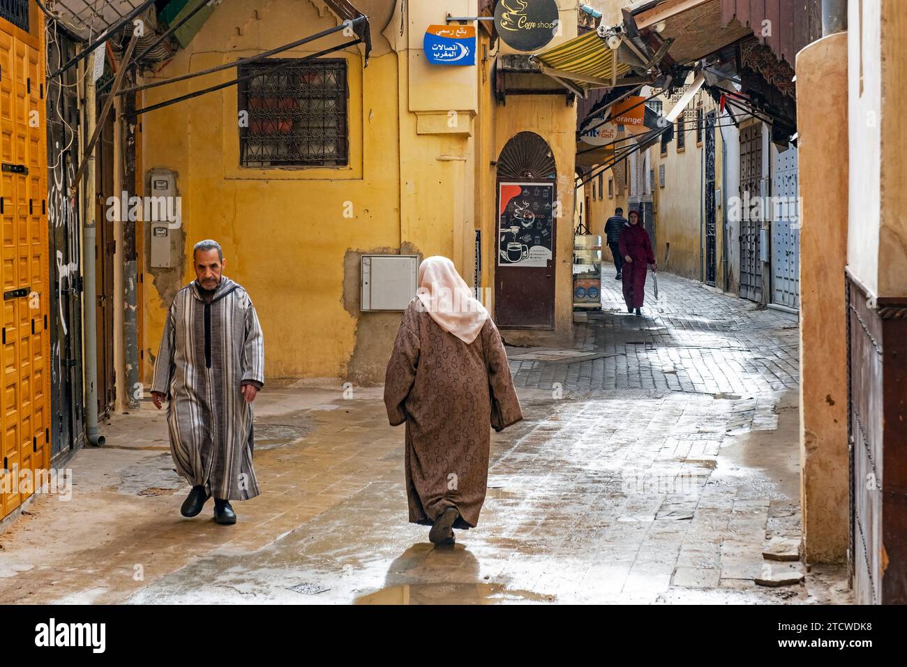 Muslimische Männer und Frauen tragen Djellabas / Jillabas an einem regnerischen Tag in der Gasse der gelben Medina der Stadt Meknes, Fes-Meknes, Marokko Stockfoto