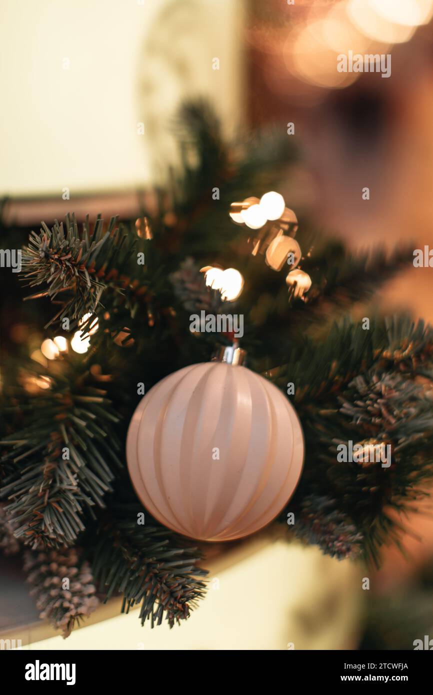 Weiße, glänzende Weihnachtskugel hängt an einem Weihnachtsbaum mit zauberhaften Lichtern. Dekorierte Fichtenzweige Stockfoto