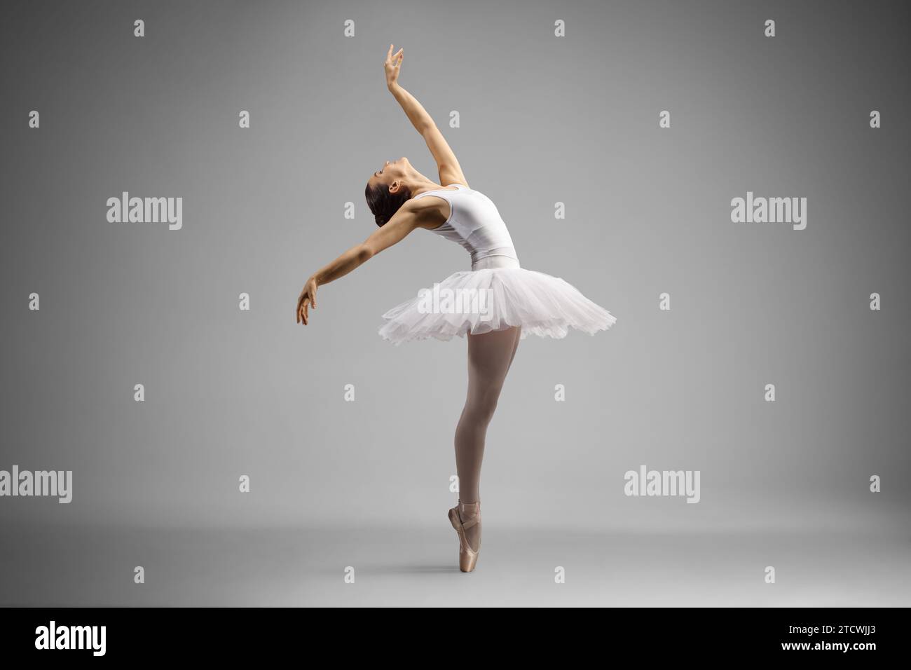 Aufnahme einer Ballerina in voller Länge, die auf grauem Hintergrund tanzt und sich nach hinten lehnt Stockfoto
