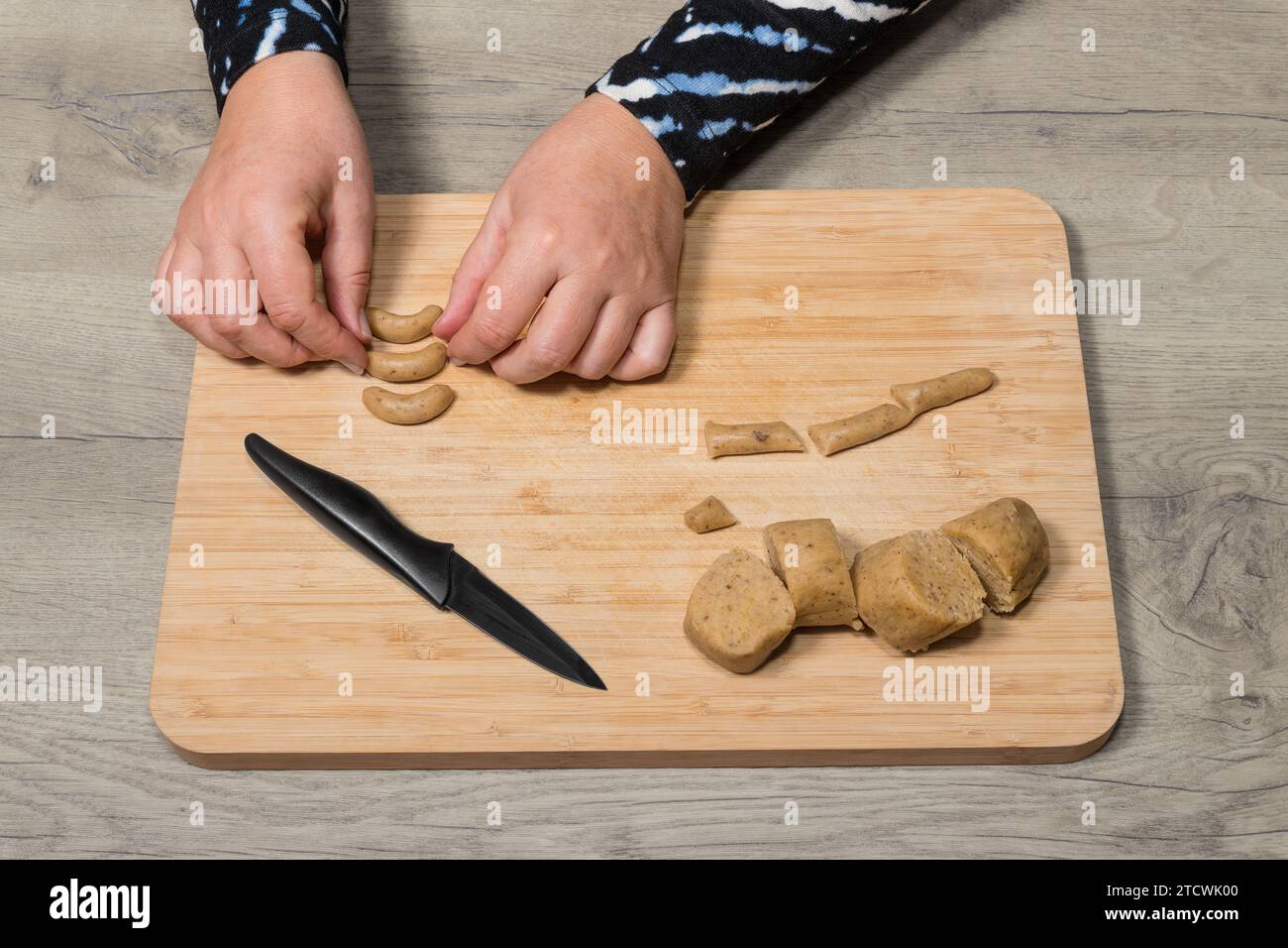 Nahaufnahme: Formende süße Kekse, Vanillerollen aus rohen nussigen Teig auf hölzernem Schneidebrett. Mit weiblichen Händen lassen sich traditionelle abgerundete Kekse Formen. Stockfoto
