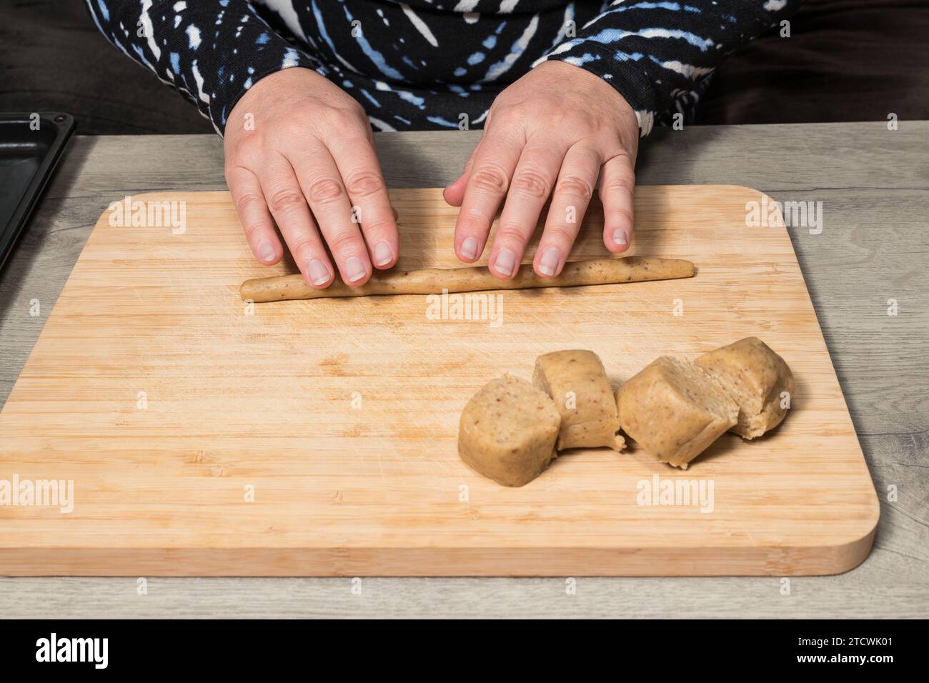 Nahaufnahme menschlicher Hände, die mit rohem nussigem Shortbread-Teig auf Holzrollbrett arbeiten. Zubereitung von leckeren süßen Keksen Vanillebrötchen. Tschechische Küche. Stockfoto