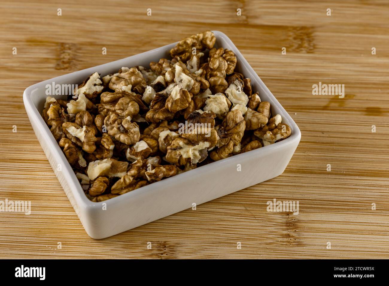 Geschälte Nüsse in einer Porzellanschale auf einem hölzernen Schneidebrett, Nüsse für Teig Stockfoto