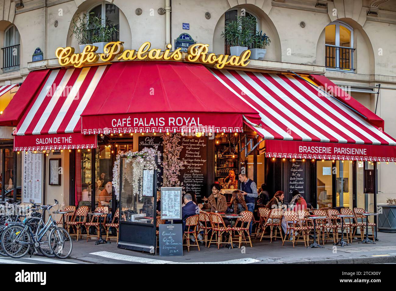 Leute sitzen draußen auf der Terrasse im Cafe Palais Royal, einem Eckbistro in der Rue Saint-Honoré, im 1. Arrondissement von Paris, Frankreich Stockfoto